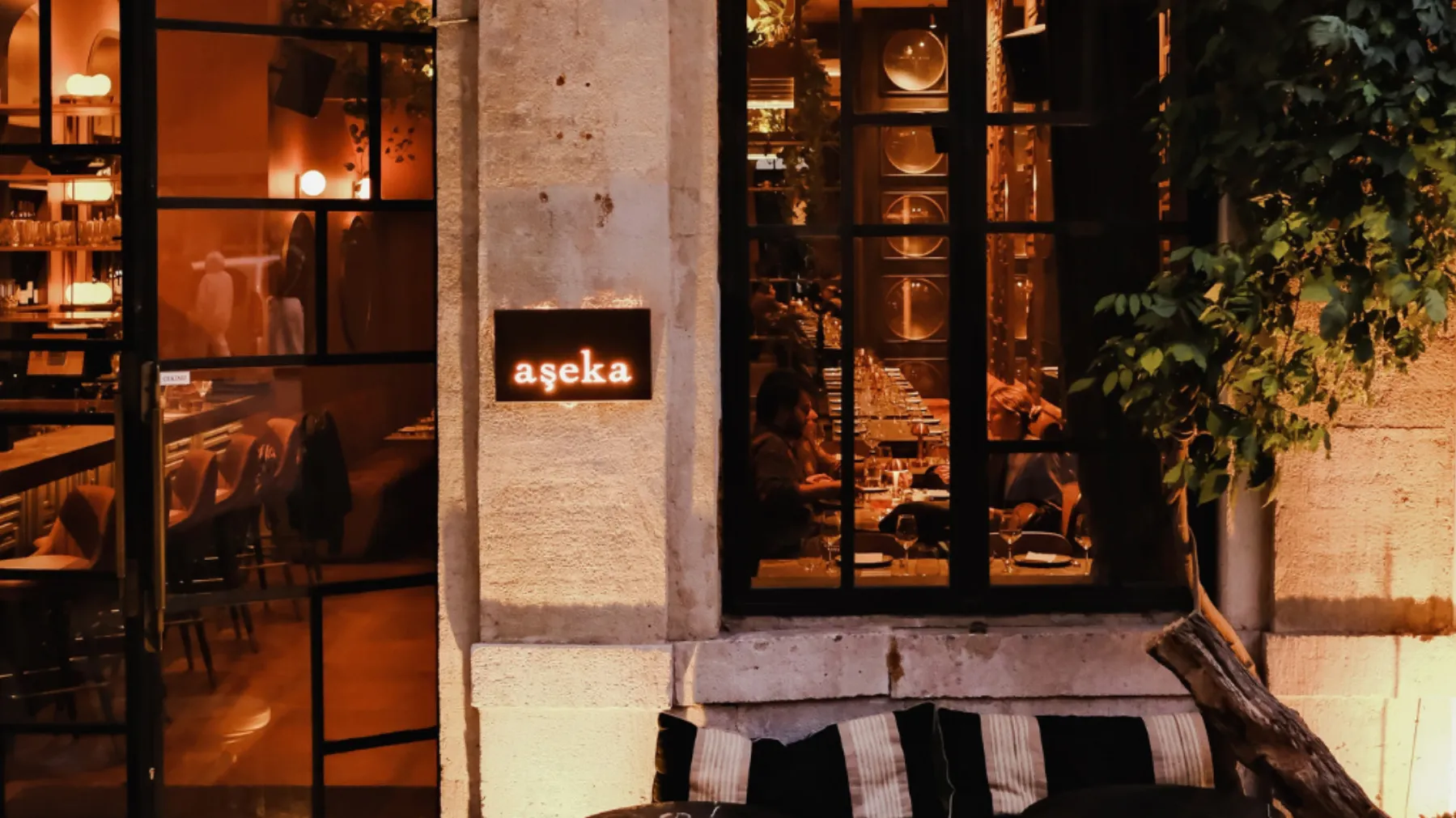 Aşeka's lit sign on a stone façade, diners seen through tall windows at night, Karaköy