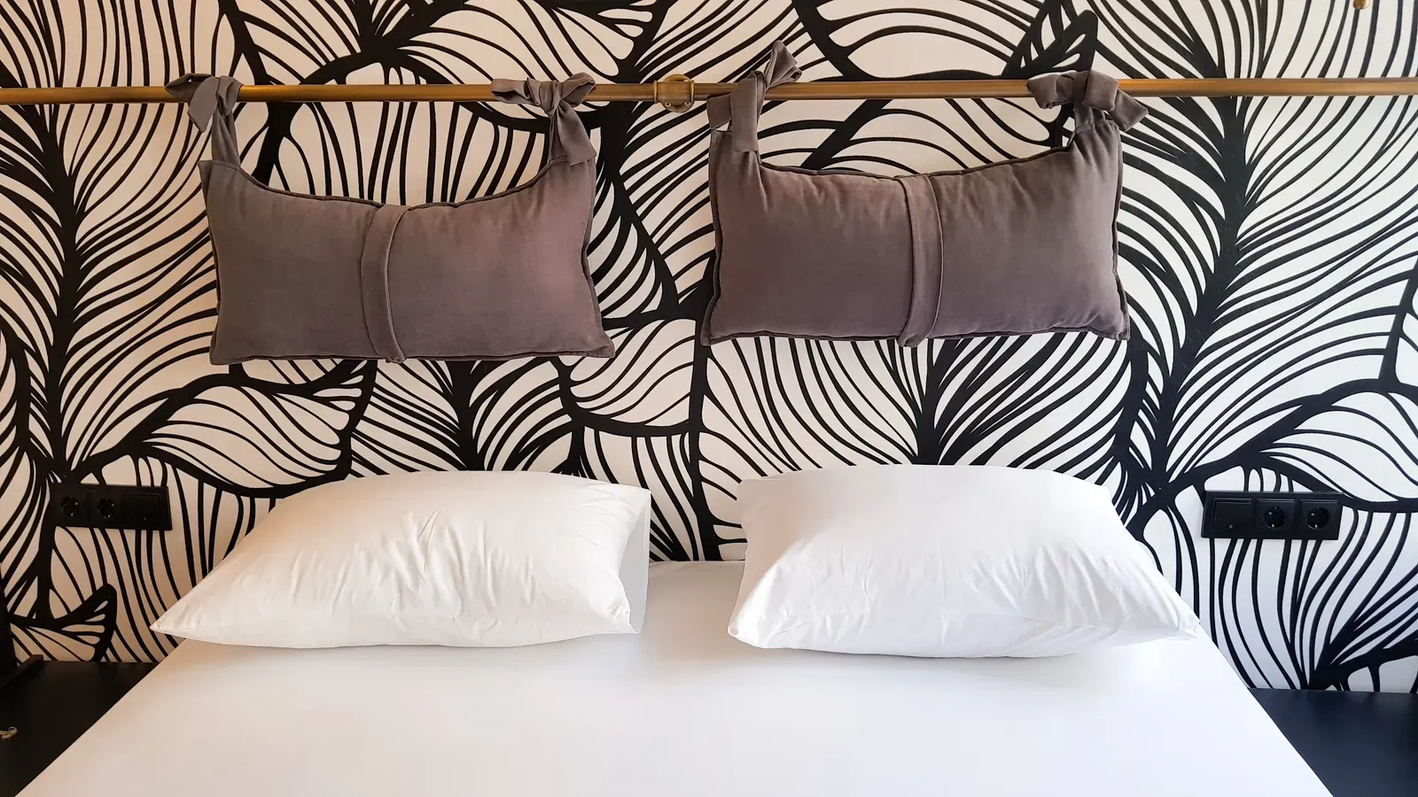 Grey bolster cushions on a brass rail above the bed in a Design Room, Karaköy, Istanbul